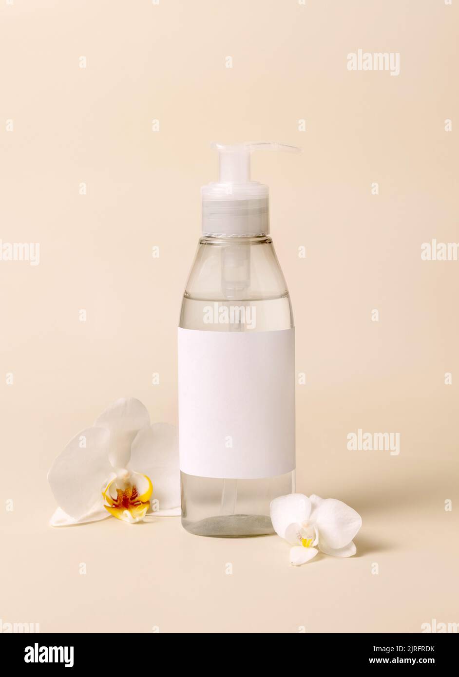 Kosmetikpumpen-Spenderflasche in der Nähe von weißen Orchideenblüten auf hellbeige Nahaufnahme, Mockup. Hautpflege Beauty-Produkt-Paket. Exotische Naturkosmetik, p Stockfoto