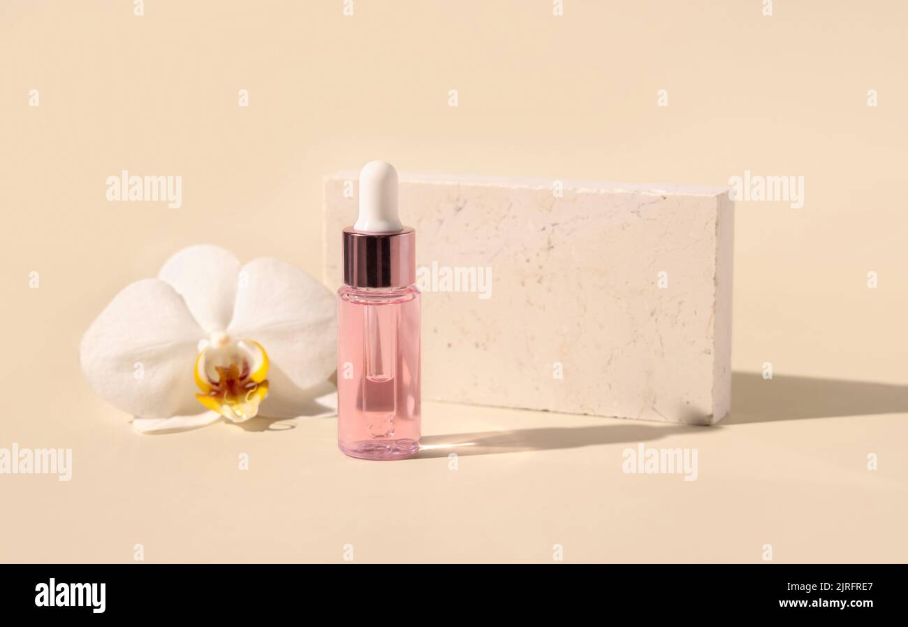 Hellrosa Tropfflasche mit Serum in der Nähe der weißen Orchideenblüte auf hellgelb, Nahaufnahme, Mockup. Hautpflegeprodukt, aromatisches Öl oder Serum. Exoti Stockfoto