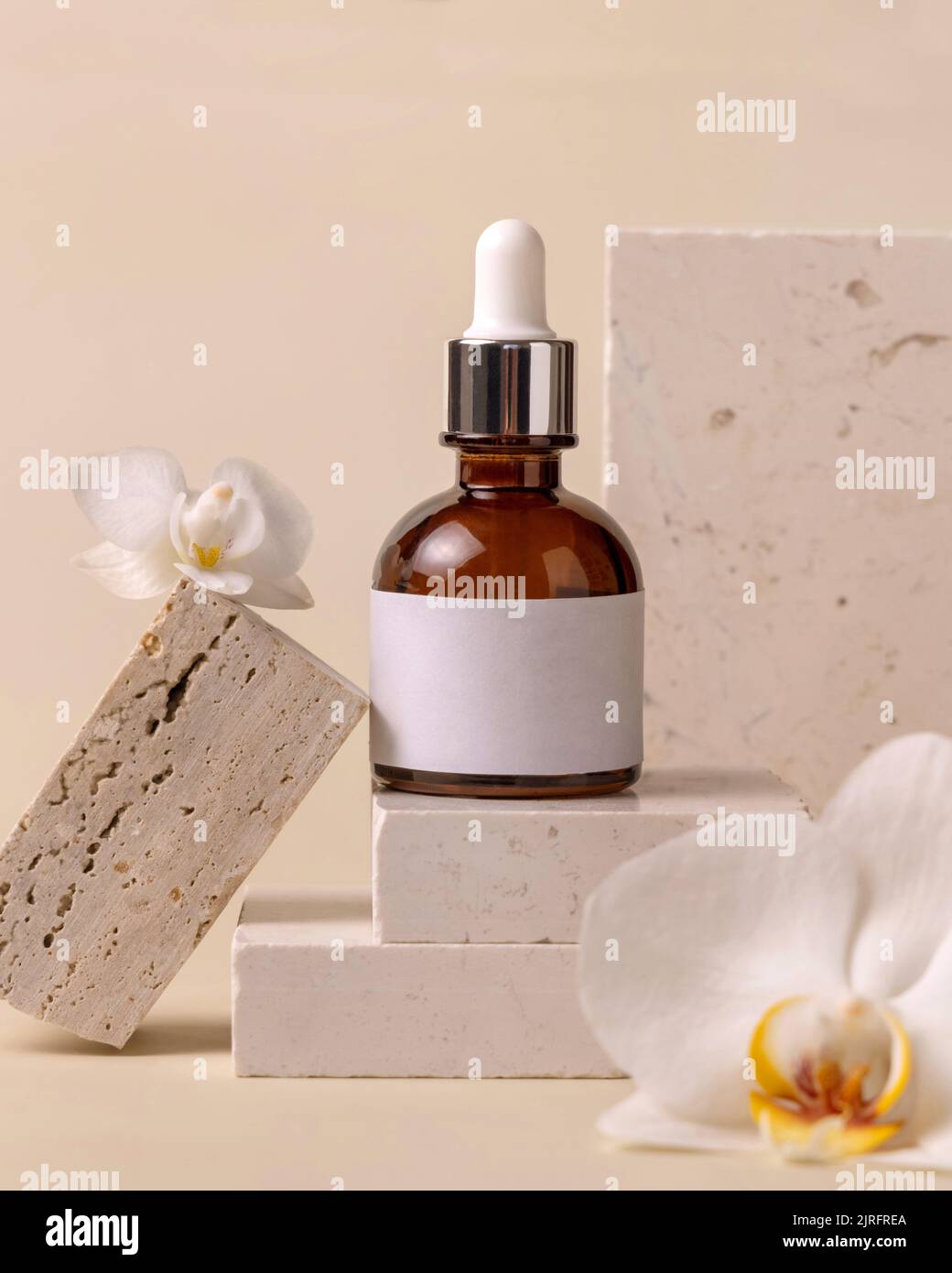Braune Glasflasche auf Stein bei weißen Orchideenblüten auf hellgelber Nahaufnahme, Etikett Mockup. Hautpflege handgemachtes Beauty-Produkt, Serum oder lotio Stockfoto