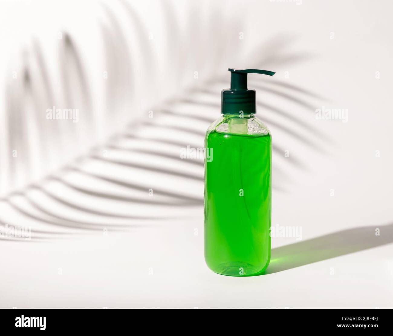 Nachfüllbare Kosmetische Pumpe Spender Flasche mit grüner Flüssigkeit auf weiß gefüllt, Palm Blatt harte Schatten, close up, mockup. Hautpflege Beauty-Produkt, Gesichtsbehandlung Stockfoto