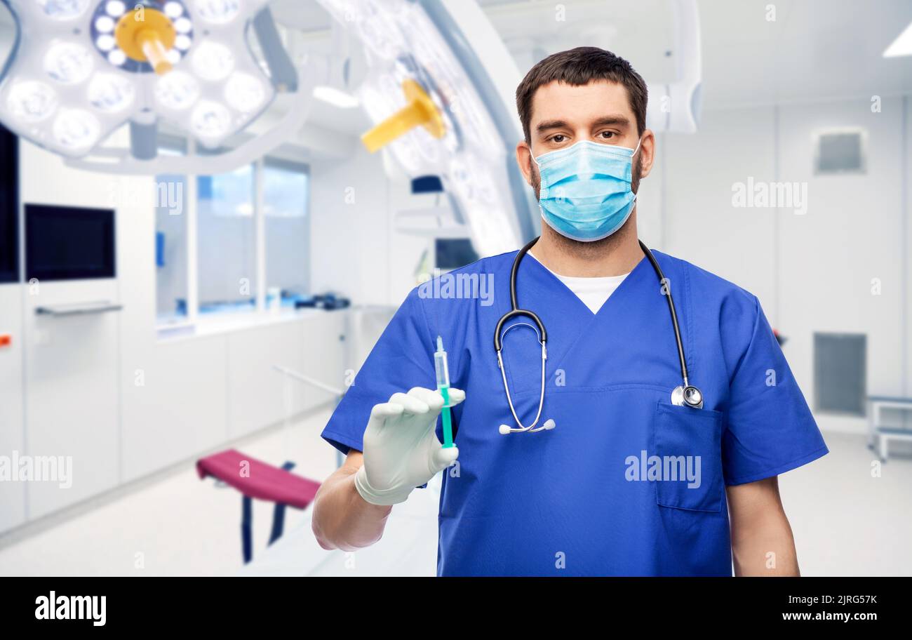 Männlicher Arzt in Maske und Handschuhe mit Spritze Stockfoto