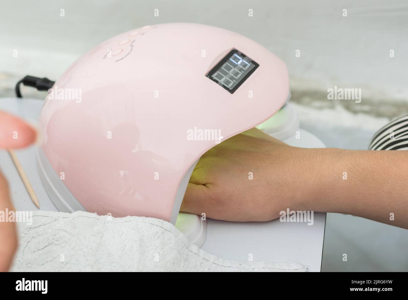 latina Frau, die ihre Hand in die LED-Lampe legt, um ihre Polygelnägel schnell zu trocknen. Mädchen legt ihre Hand für kurze Zeit in die gelbe Lampe. Stockfoto