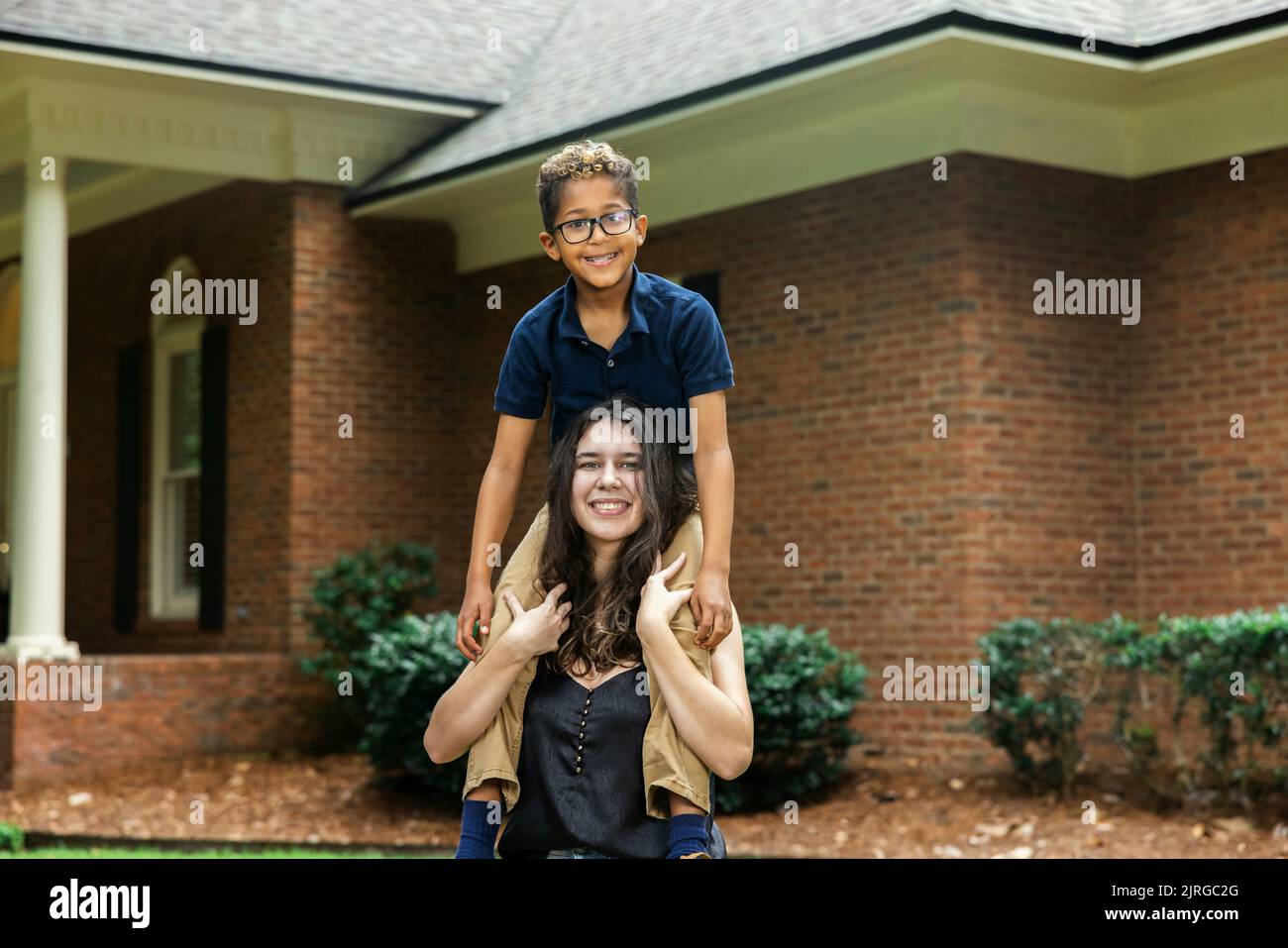 Eine große Schwester hält ihren kleinen Bruder auf den Schultern für ein lustiges Porträt Stockfoto