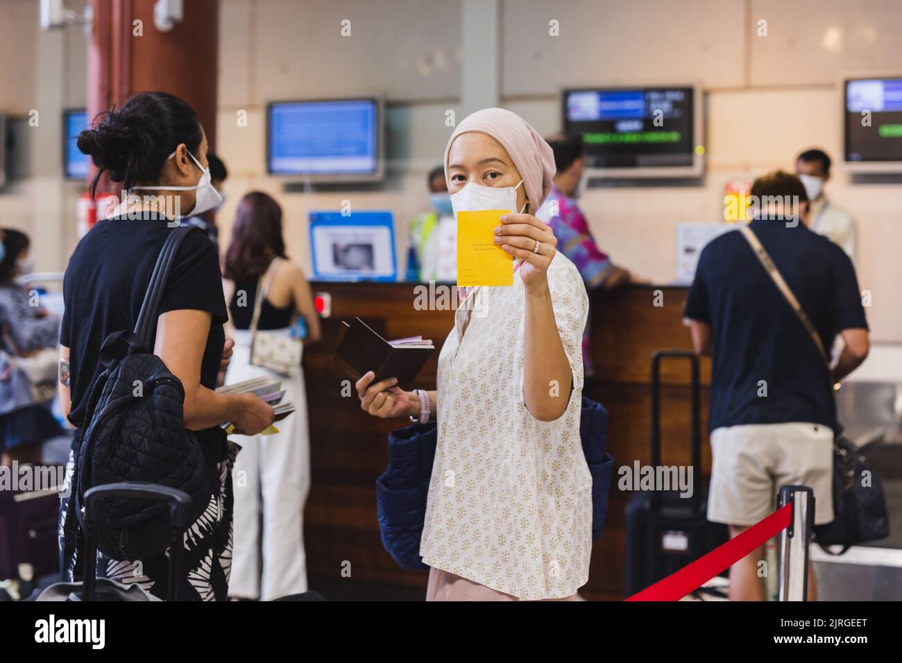 Eine Asiatin mit Gesichtsmaske checkt am Flughafen ein und zeigt ihren Impfpass. Stockfoto