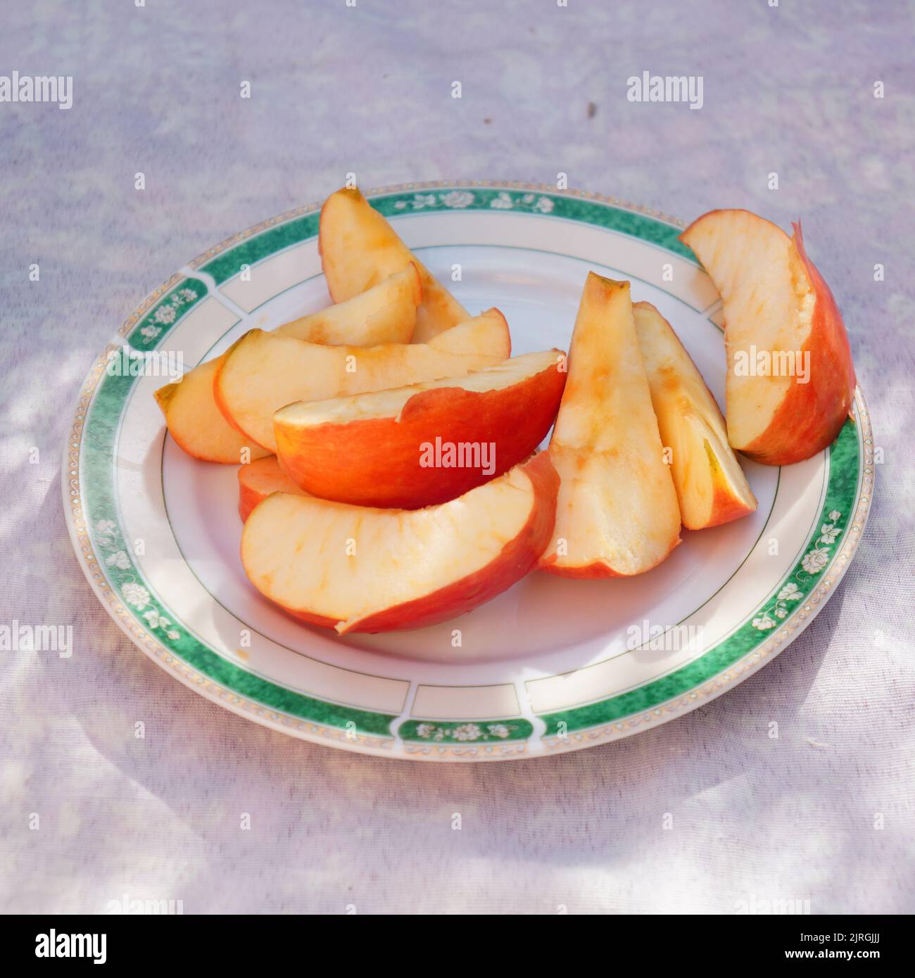 Schneiden Sie kleine Stücke eines frischen Apfels, der an einem sonnigen Tag auf einem Teller serviert wird. Stockfoto