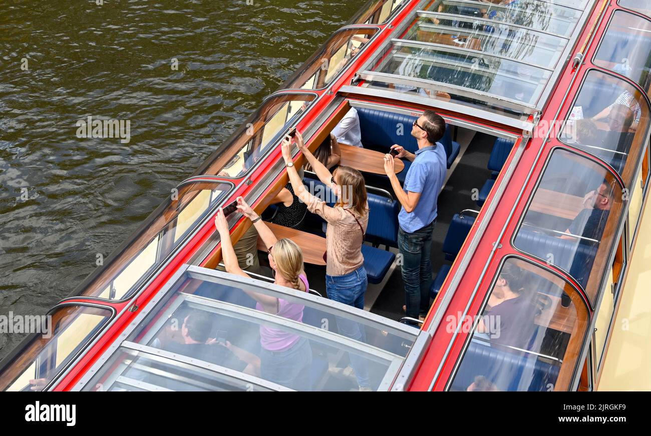 Amsterdam, Niederlande - August 2022: Menschen stehen auf, um Fotos von einem Touristenboot auf einem der Kanäle der Stadt zu machen. Stockfoto