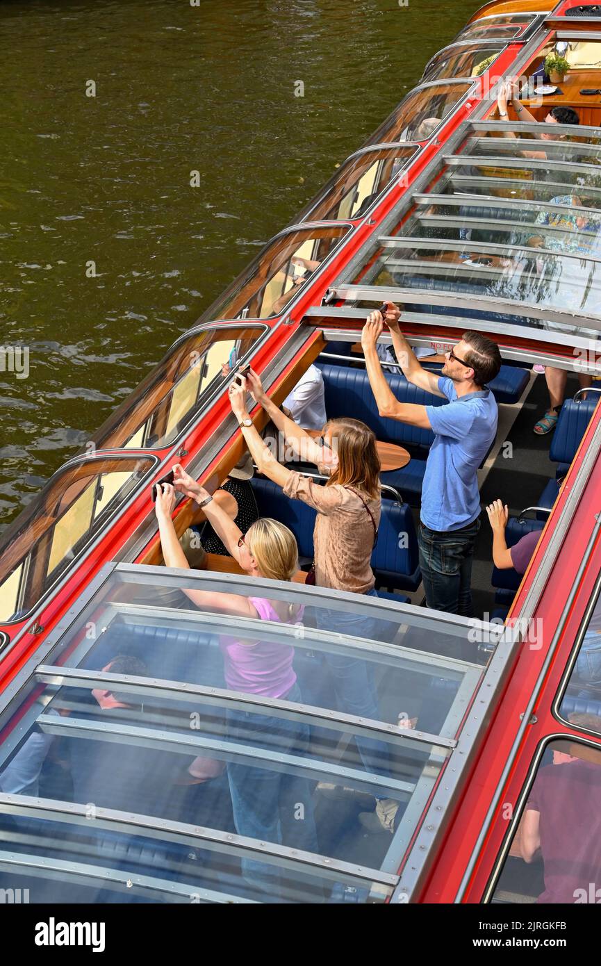 Amsterdam, Niederlande - August 2022: Menschen stehen auf, um Fotos von einem Touristenboot auf einem der Kanäle der Stadt zu machen. Stockfoto