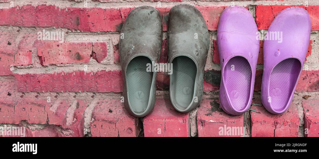 Zwei Paar Gummi-Galoschen in Schwarz und Pink auf dem Hintergrund einer alten Ziegelwand, eine Kopie des Raumes auf der linken Seite Stockfoto