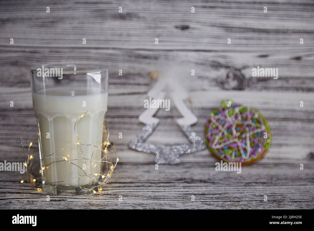 Süße Weihnachtstradition. Handgemachte frische Kekse und Glas mit Milch für den Weihnachtsmann auf dem Vintage-Holztisch. Festliche Weihnachtsstimmung und ästhetische Atmosphäre mit Girlanden Hintergrund. Speicherplatz kopieren. Stockfoto