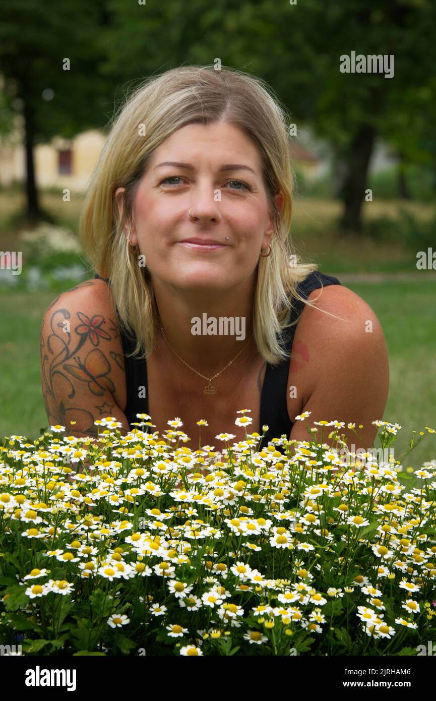 Porträt einer blonden Frau hinter schönen Gänseblümchen-Blumen in gelb-grünen Farben Stockfoto