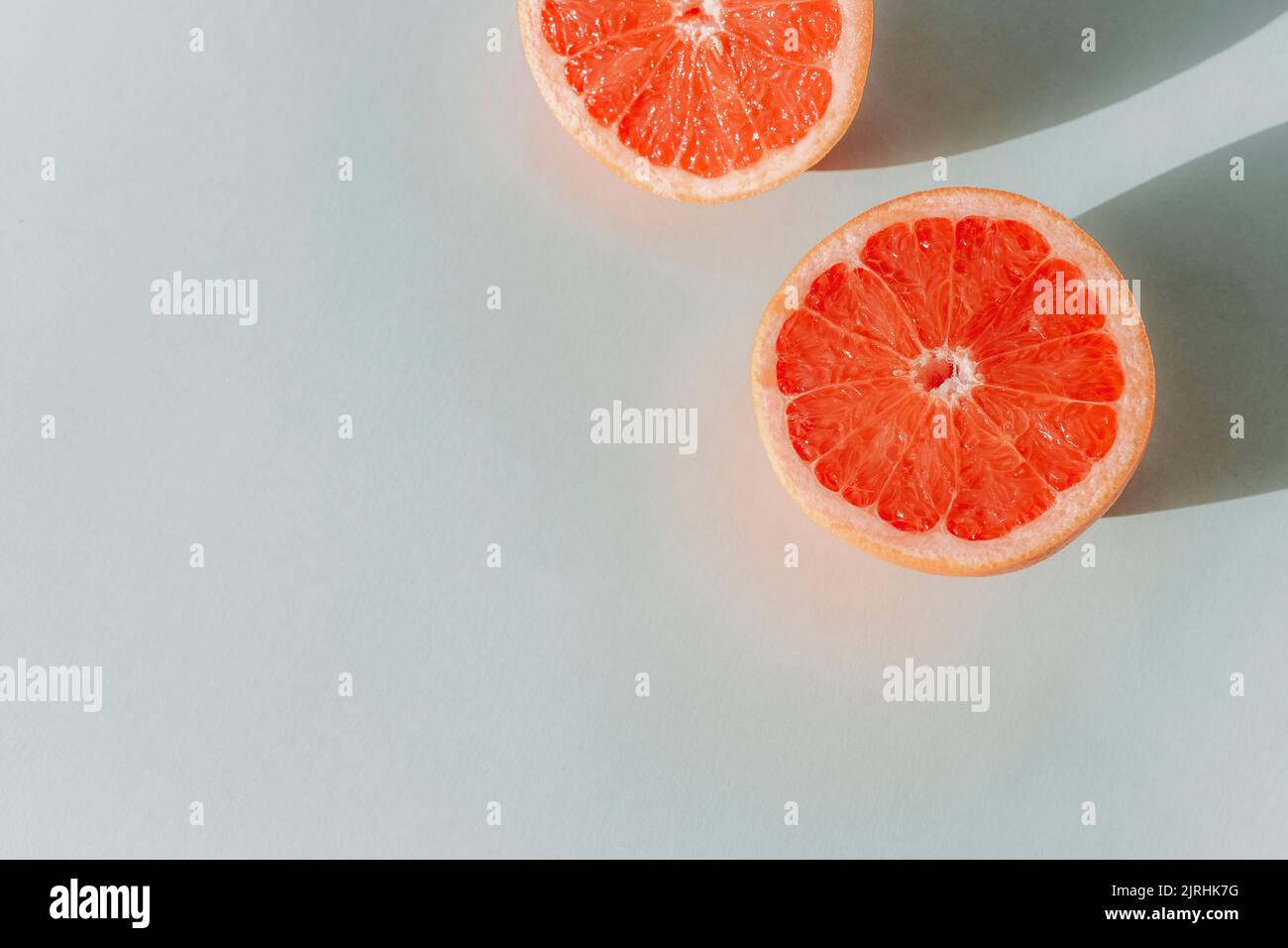 Rote Grapefruitscheiben mit harten Schatten auf blauem Hintergrund. Draufsicht, flach liegend, Kopierbereich. Stockfoto