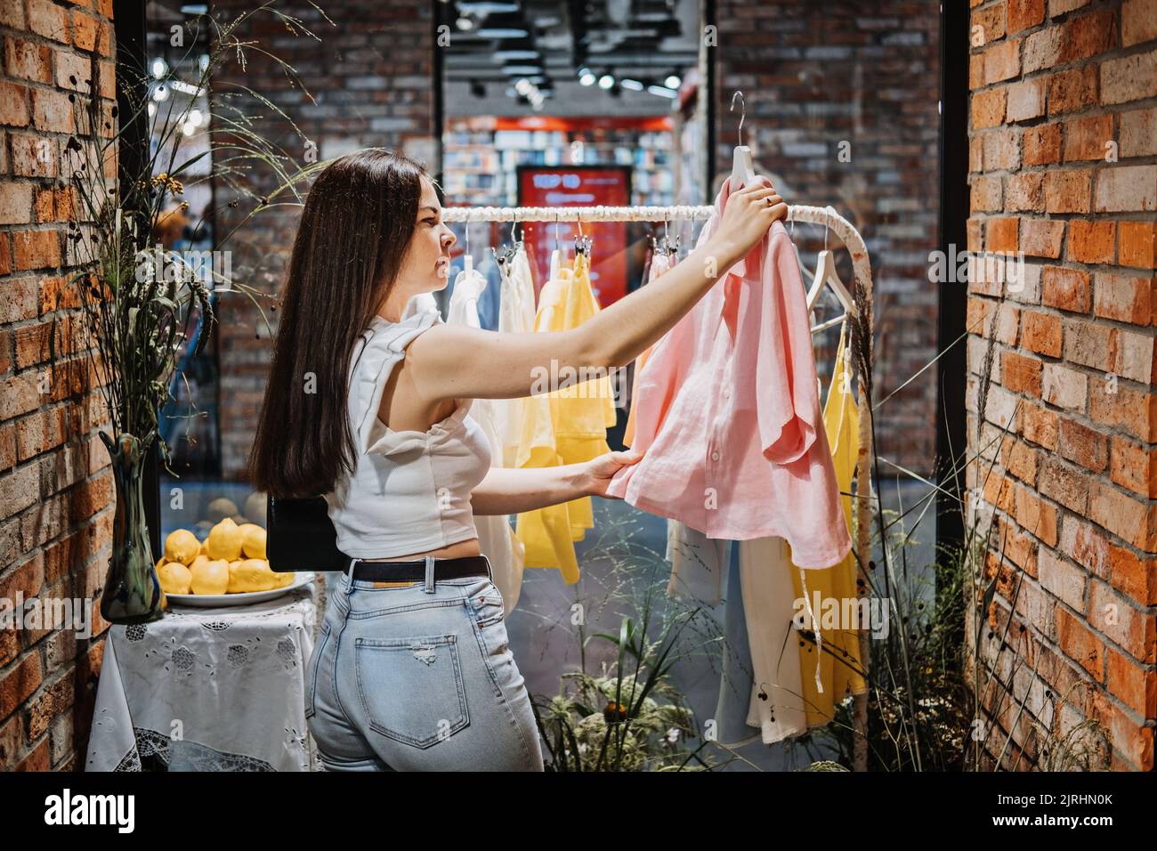 Moderne junge Latina-Frau, die sich für Bio-Leinenbekleidung und T-Shirt im modernen, umweltfreundlichen Laden im Einkaufszentrum entscheidet Stockfoto