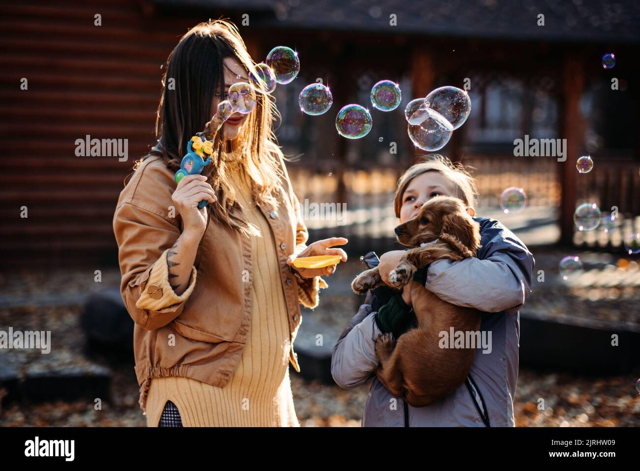Glückliche Familie Mutter und Teenager Junge Sohn mit niedlichen Cocker Spaniel Welpen blasen Seifenblasen im Freien im Herbst Park. Stockfoto