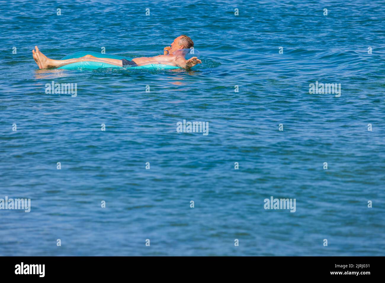 Nahaufnahme des Mannes auf aufblasbarer Matratze auf blauer Wasseroberfläche. Rhodos. Griechenland. Stockfoto