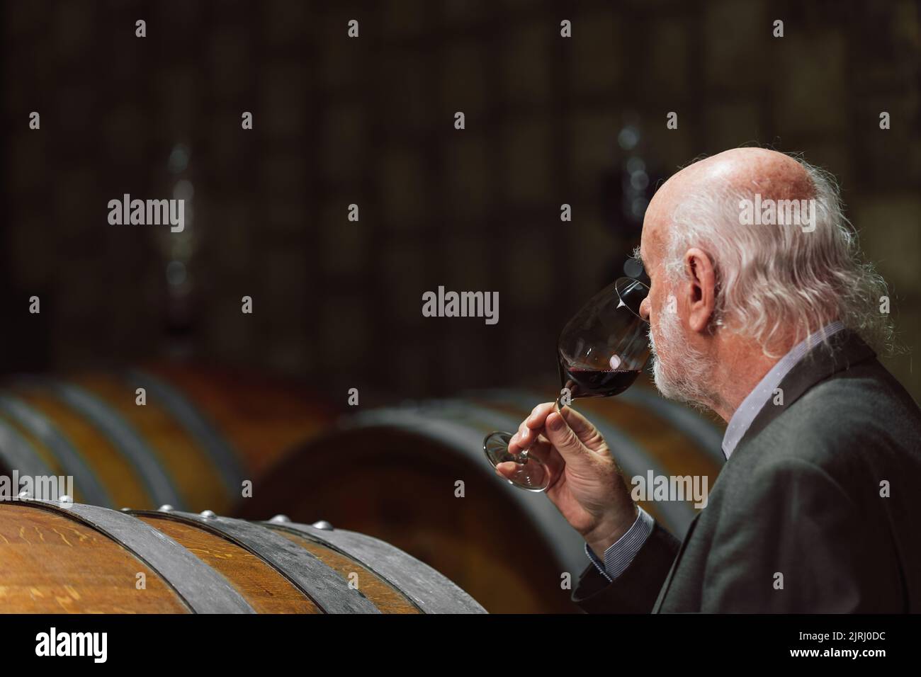 Älterer kaukasischer Tourist, Graubart eleganter Mann, der Rotwein in einem unterirdischen Weinkeller des Weinguts mit einer langen Tradition verkostet Stockfoto