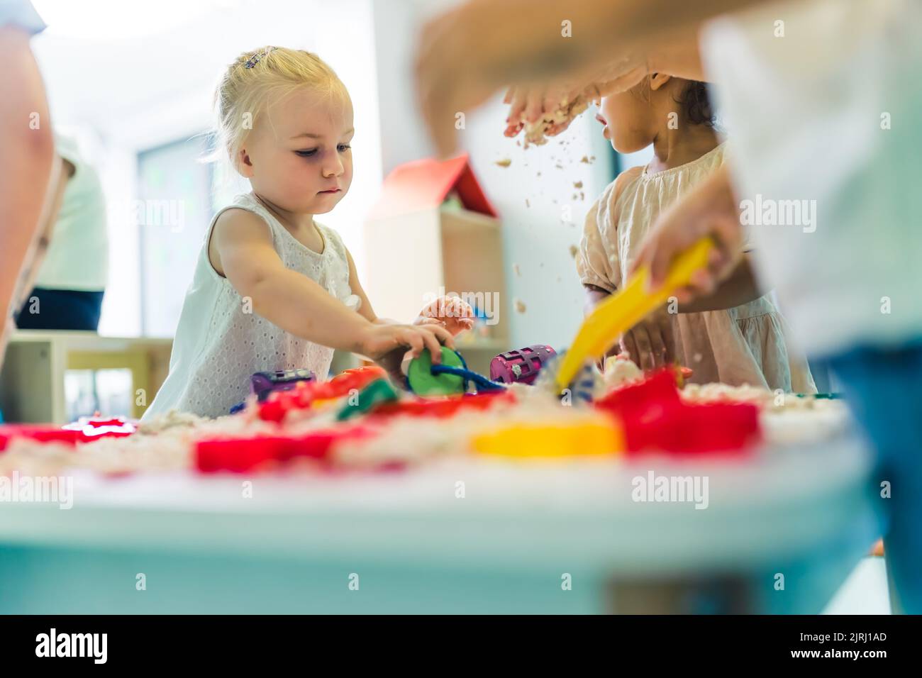 Kreatives Sinnesspiel mit formbarem und flauschigen kinetischen Sand im Kindergarten. Kleinkinder stehen um den Tisch herum und verwenden verschiedene Werkzeuge zum Formen von Sand wie bunte und strukturierte Rollnadeln, Schneideplotter, Silikon-Formausschnitte. Feinmotorik und Entwicklung der Hand-Auge-Koordination. Hochwertige Fotos Stockfoto