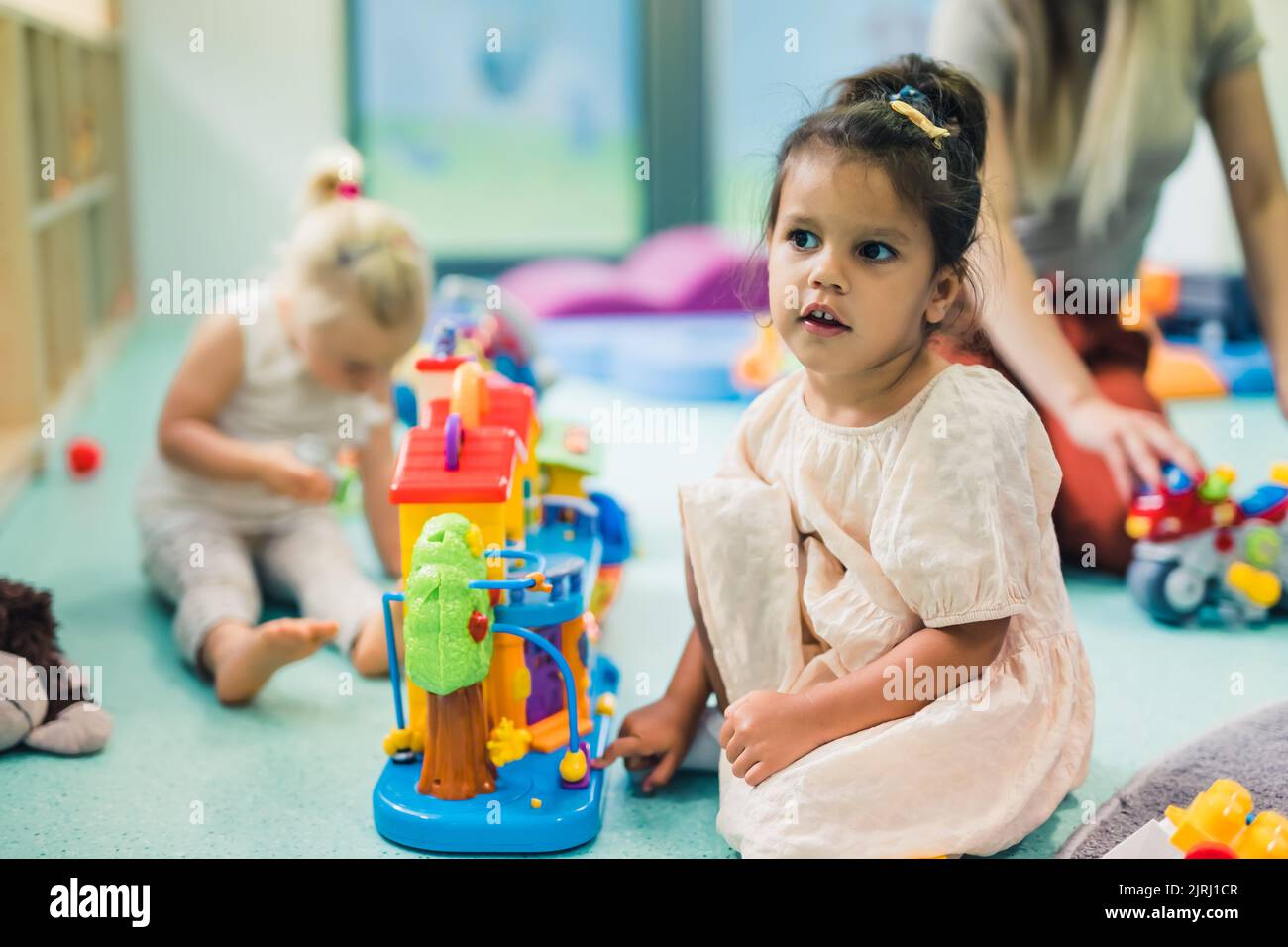 Spielerisch im Kindergarten lernen. Kleinkind kleines Mädchen und die Lehrerin spielen mit bunten Kunststoff-Spielhäusern, Bausteinen, Autos und Booten. Entwicklung von Phantasie, Kreativität, Feinmotorik und grobmotorischen Fähigkeiten. Hochwertige Fotos Stockfoto