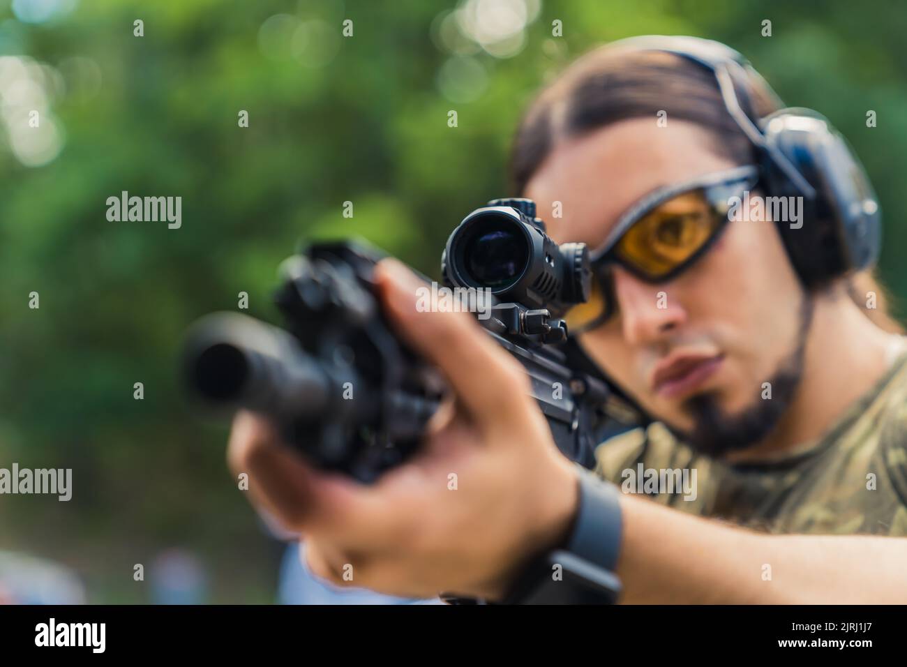 Nahaufnahme eines kaukasischen, dunkel angeheuerten Militärs mittleren Alters in schützendem Schießstand, der durch die Lupe seines Gewehr schaute. Verschwommener grüner Hintergrund. Hochwertige Fotos Stockfoto