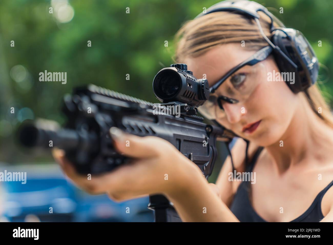 Nahaufnahme einer Lupe eines schwarzen Gewehr, das von einer fokussierten, mächtigen kaukasischen Frau in schützendem Schießstand gehalten wird. Unscharfer Hintergrund. Hochwertige Fotos Stockfoto