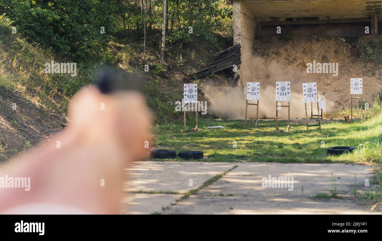 Zwei verschwommene Hände einer nicht erkennbaren kaukasischen Person, die mit einer schwarzen Waffe auf Papierziele zielte. Reichweite der Außenpistolen. Schusswaffenkonzept. Hochwertige Fotos Stockfoto