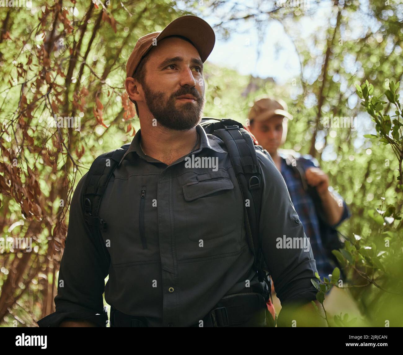 Freunde wandern in der Natur, während sie gemeinsam in einem grünen Wald unterwegs sind, aktiv sind und sich im Freien verbinden. Männlich zu Fuß auf dem Weg in den Wald Stockfoto