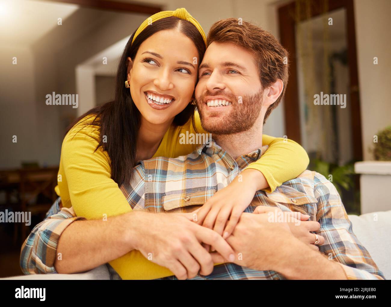 Glückliches und aufgeregt Paar umarmt denken Zukunft entspannen und sitzen auf einer Couch zu Hause. Entspannte, vielfältige interracial Liebhaber lächeln und genießen Stockfoto