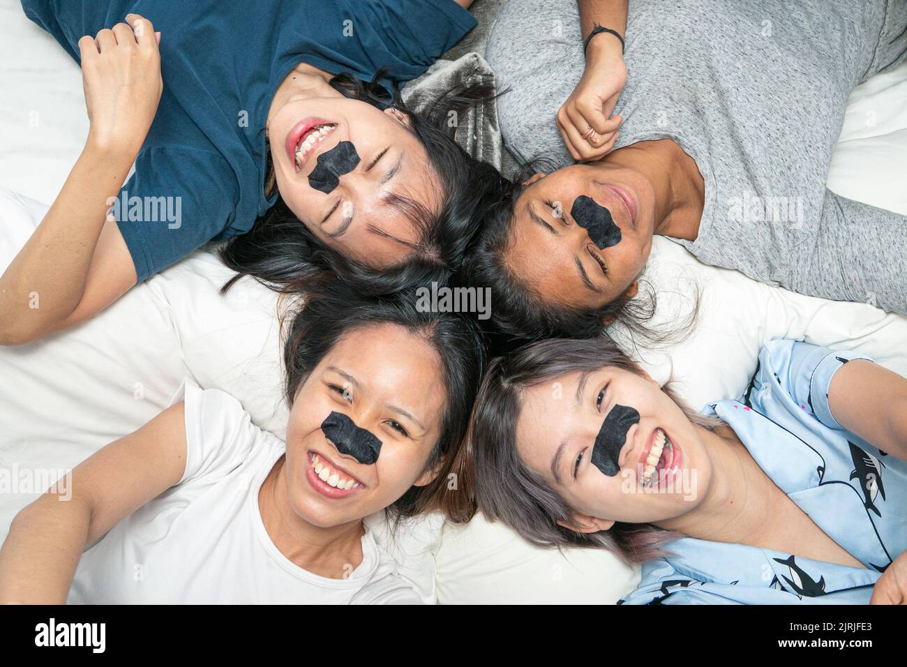 Glückliche attraktive multiethnische asiatische junge Frauen mit Poren-Streifen, auf dem Bett liegend. „Sleep over Party“-Konzept. Draufsicht. Stockfoto