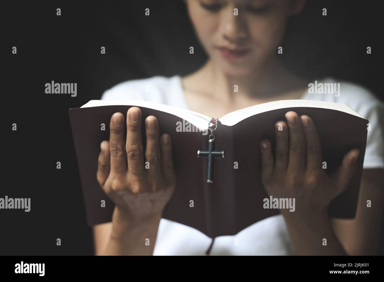 Die Schrift und das Kreuz werden von einer ehrlichen und christlichen jungen Frau gelesen, um Ideen zu beten, zu glauben, zu glauben, zu beten, zu wünschen. Stockfoto