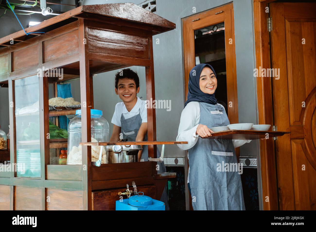 muslimische Verkäufer in Schürze Vorbereitung Hühnernudeln Gericht mit Schüsseln Stockfoto