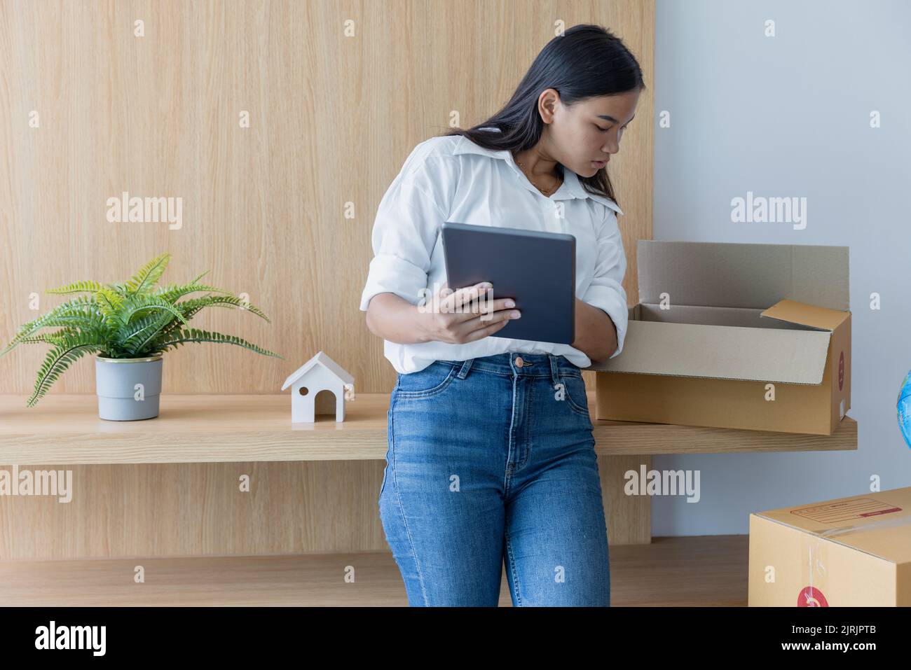 Frau, die ein Tablet hält und einen Karton überprüft.Packing stuff to move in a New House. Stockfoto