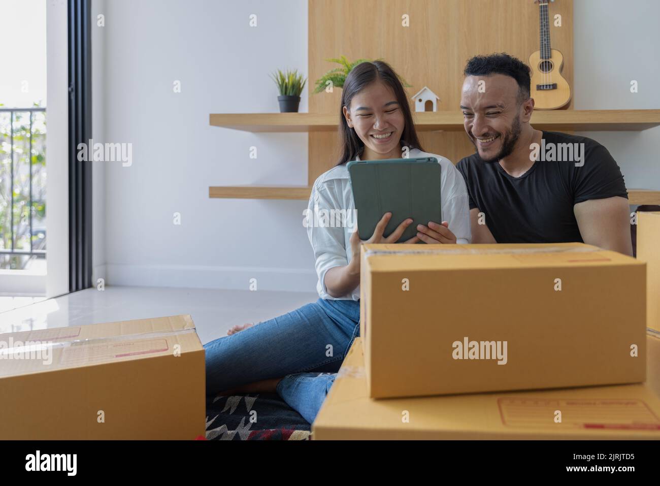 Das Konzept des Umzugshauses. Paar hält ein Tablet und prüft einen Karton Packmittel, um in ein neues Haus zu ziehen. Stockfoto