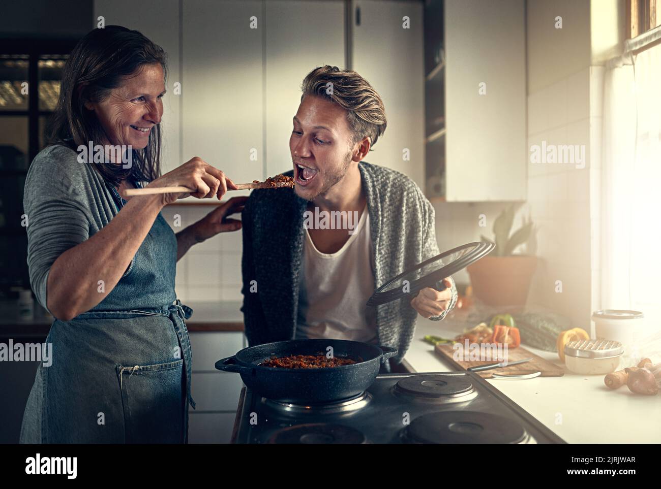 Essen nur eine Mutter kann kochen. Mutter gibt ihrem erwachsenen Sohn einen Vorgeschmack auf das, was sie in der Küche kocht. Stockfoto