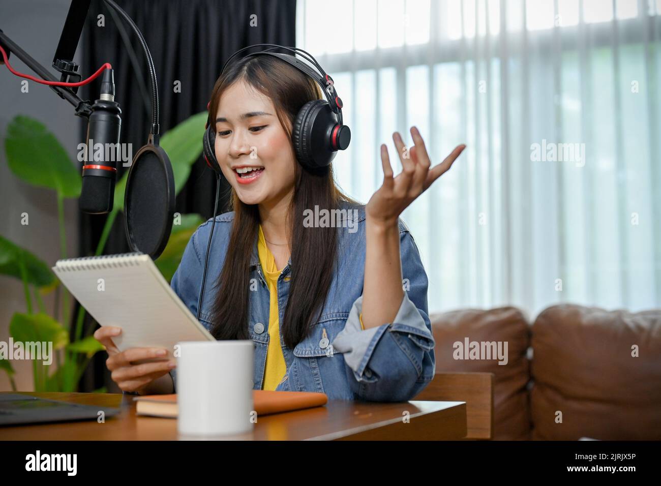 Happy Asian girl nehmen einen Podcast mit Kopfhörern und Mikrofon auf. Weibliche Podcasterin macht Audio-Podcast aus ihrem Heimstudio. Stockfoto