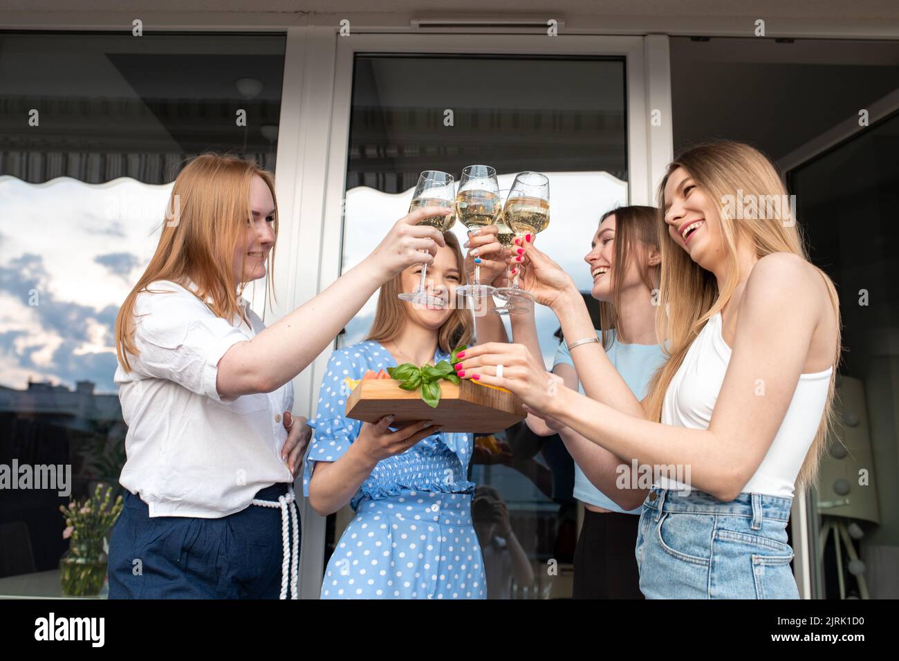 Porträt von jungen, glücklichen, gutaussehenden Frauen, die Gemüse, klirrende Gläser Weißwein in der Nähe des Hauses halten. Stockfoto