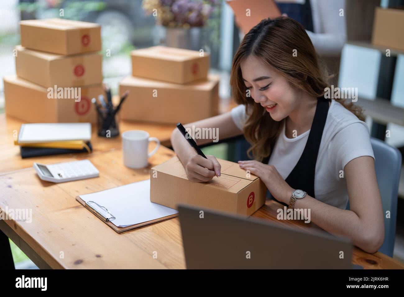 Die Frau, die ein kleines Startup-Unternehmen in einem Büro führt, arbeitet an einem Laptop und Boxen für die Verpackung und Vorbereitung von Artikeln für den Versand. Stockfoto