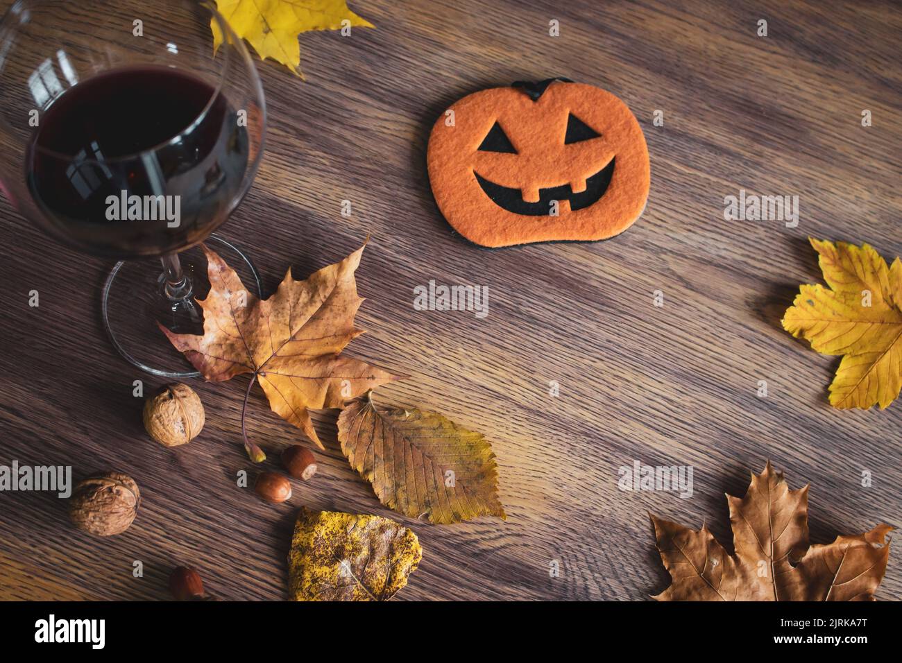 Halloween Stillleben. Ein Glas Rotwein, Nüsse, trockene Blätter und lustige Kürbisfigur auf dem Tisch. Herbstferien. Oktober Hintergrund. Stockfoto