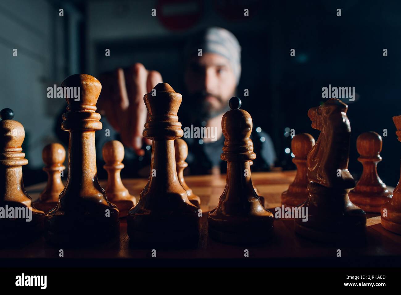 Junger, hübscher Mann, der im Dunkeln Schach spielt und seitlich beleuchtet ist. Stockfoto