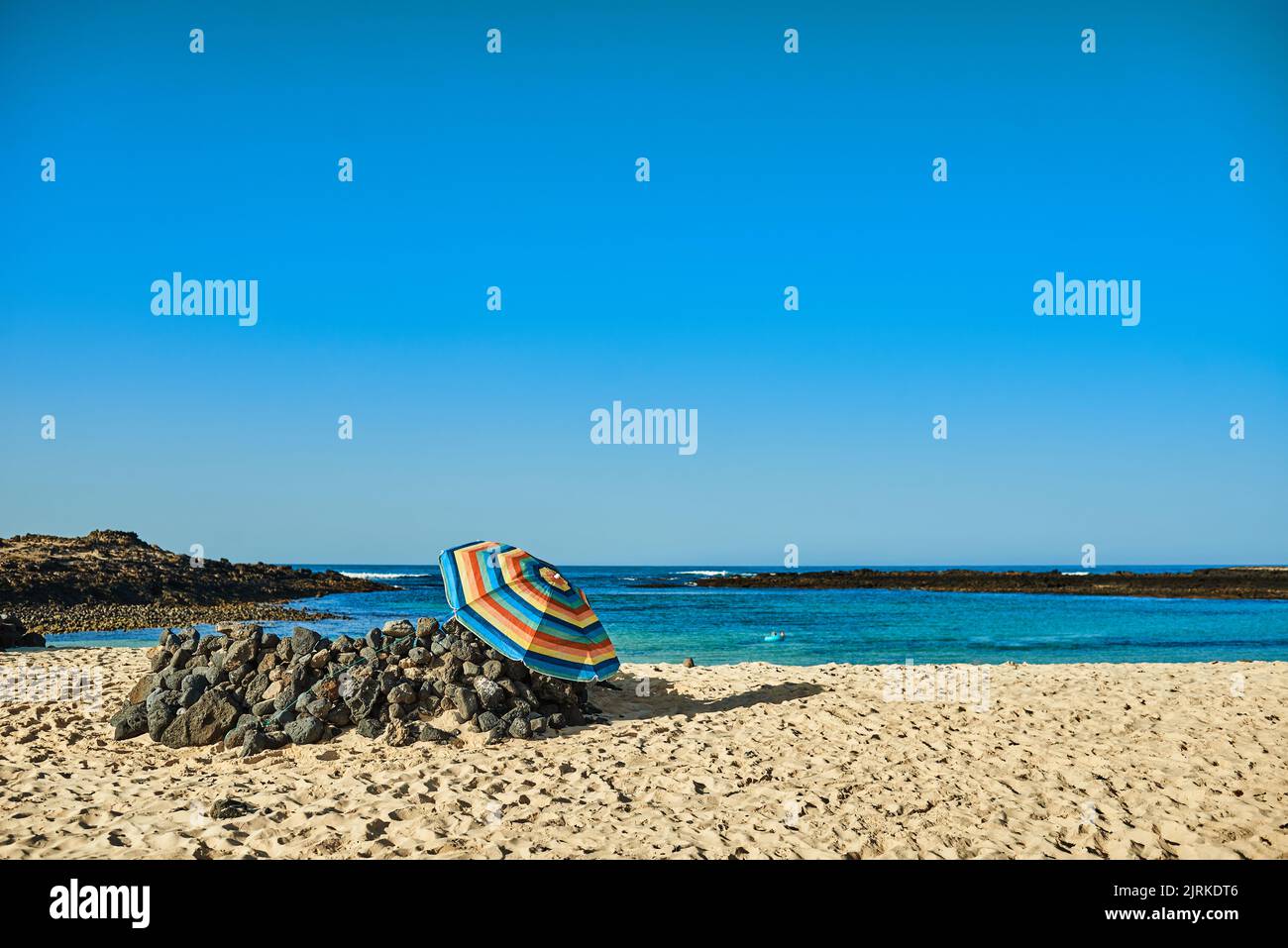 Spektakulärer Blick auf ornamentalen Sonnenschirm in der Nähe von Steinen an der Küste gegen blaues Meer mit Horizont in Fuerteventura Spanien Stockfoto