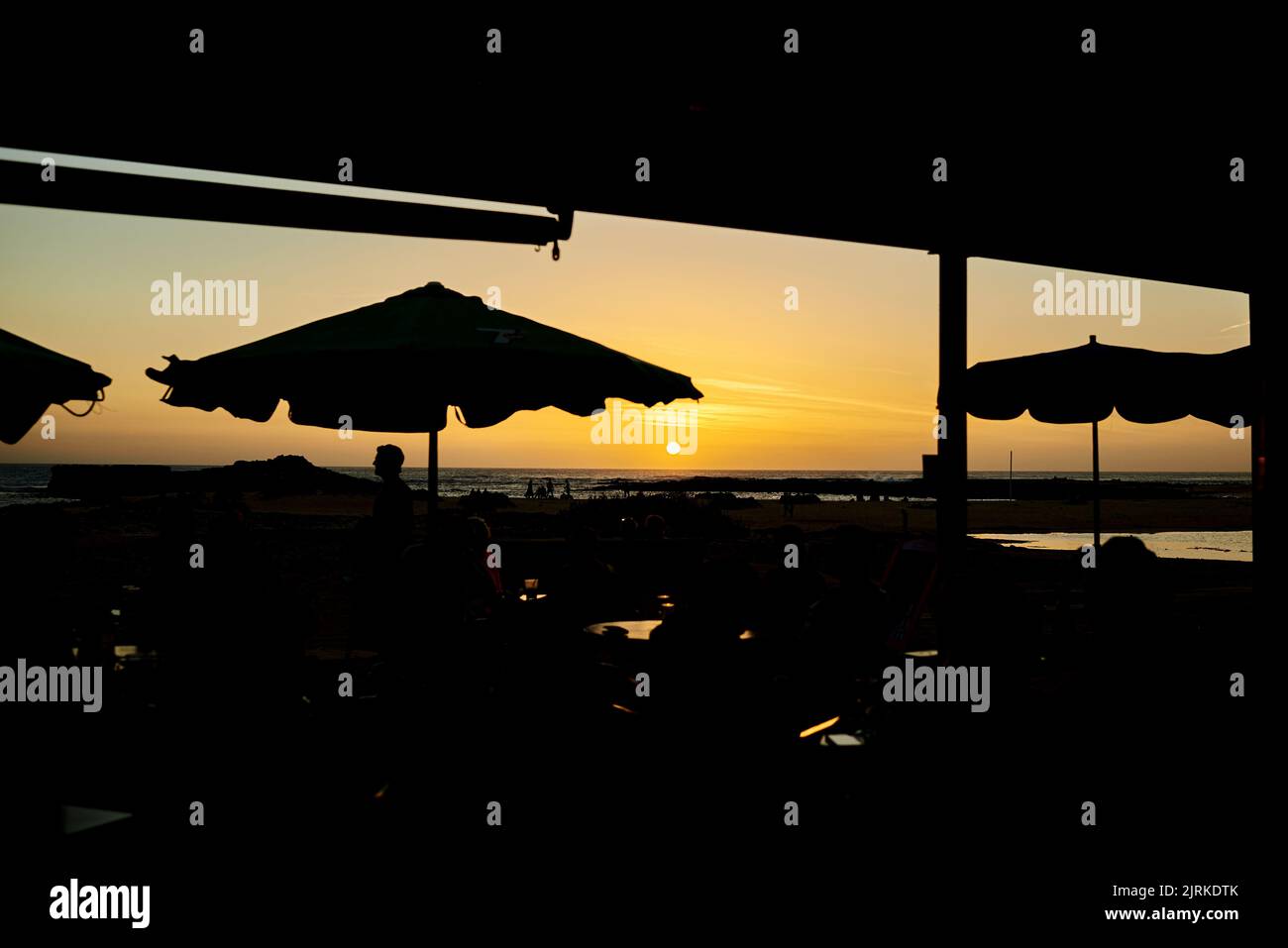 Seitenansicht der anonymen männlichen Touristen-Silhouette am Ufer unter Sonnenschutz gegen den Atlantik bei Sonnenuntergang auf Fuerteventura Spanien Stockfoto