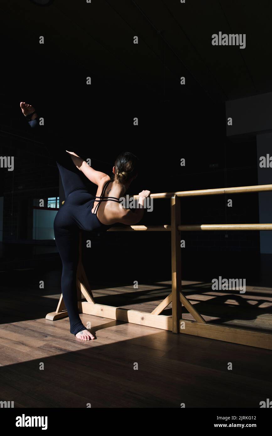 Junge Tänzerin, die eine Dehnungsroutine auf einer hölzernen Barre im Tanzstudio macht Stockfoto