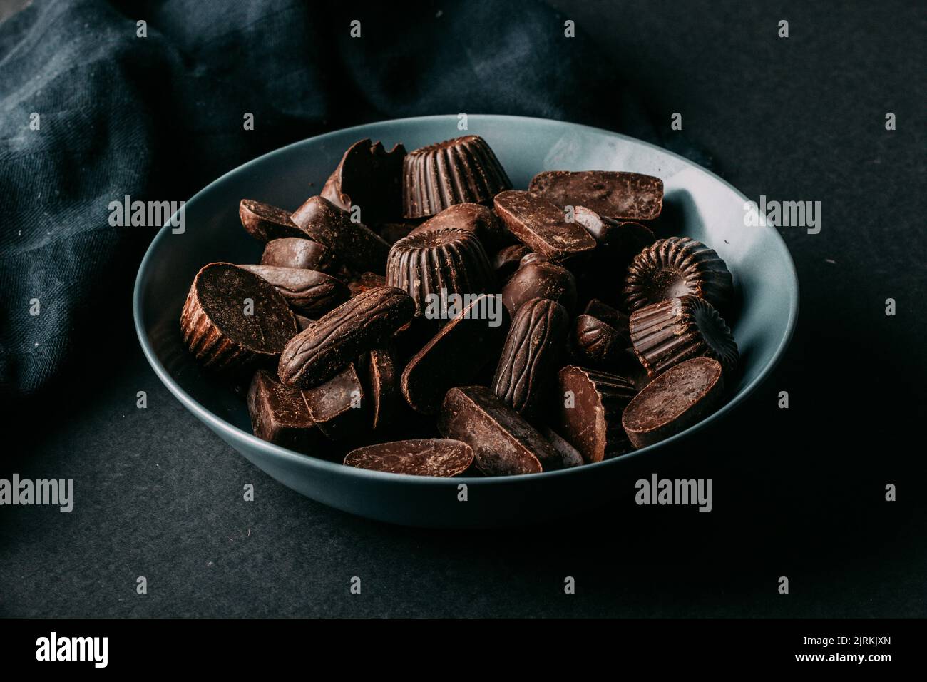 Verschiedene dunkle Schokoladentrüffel und Pralinés in verschiedenen Formen in einer Schüssel auf einem schwarzen Tisch platziert Stockfoto