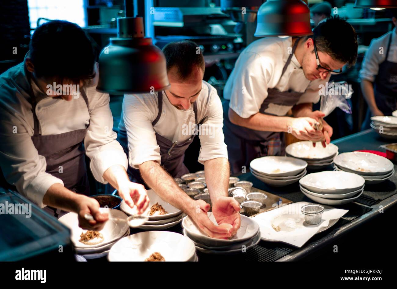 Junge Köche Männer in Schürzen sorgfältig serviert Mahlzeit in weißen Keramikgerichten in der Restaurantküche Stockfoto