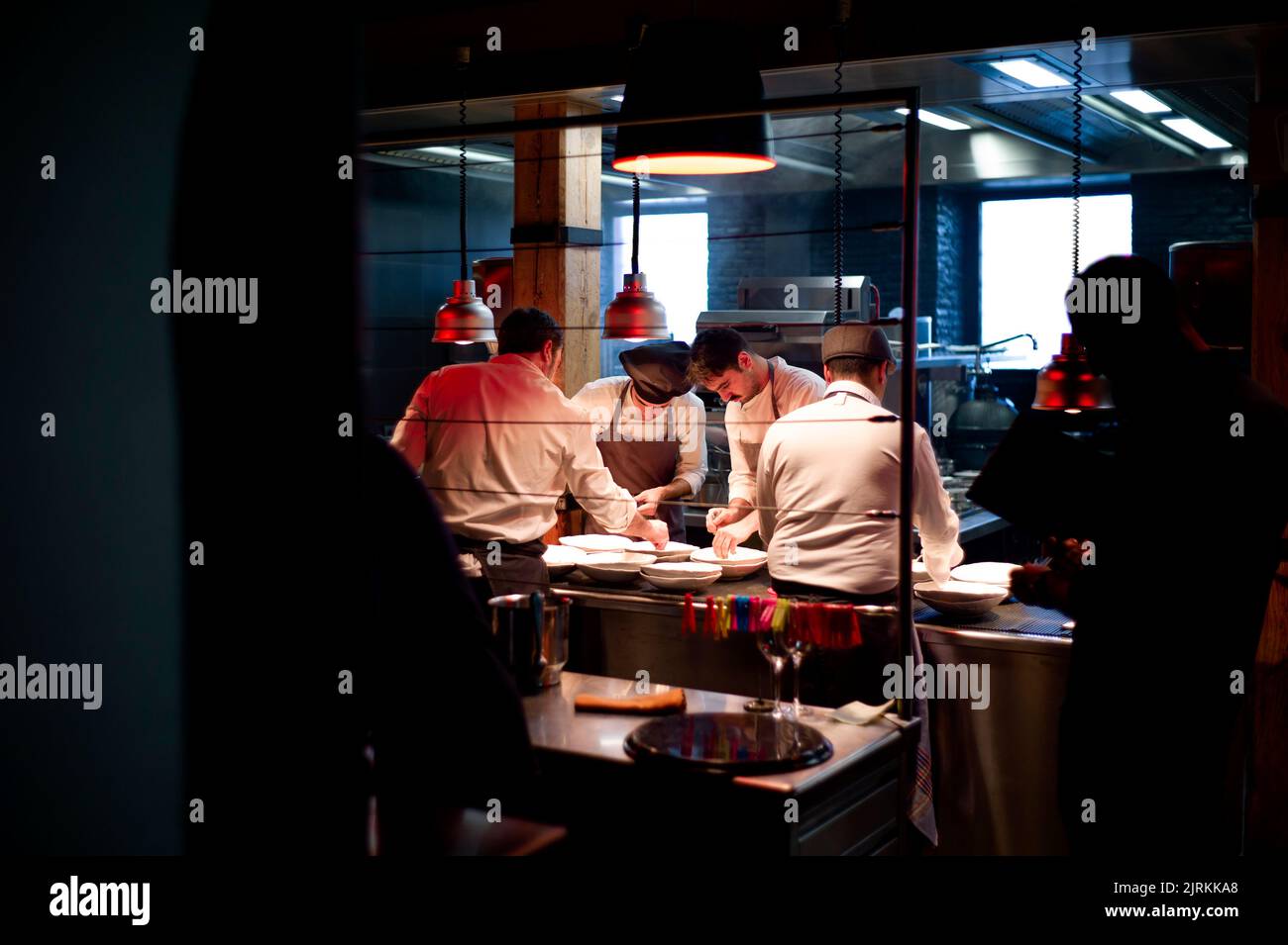 Junge Köche Männer in Schürzen sorgfältig serviert Mahlzeit in weißen Keramikgerichten in der Restaurantküche Stockfoto
