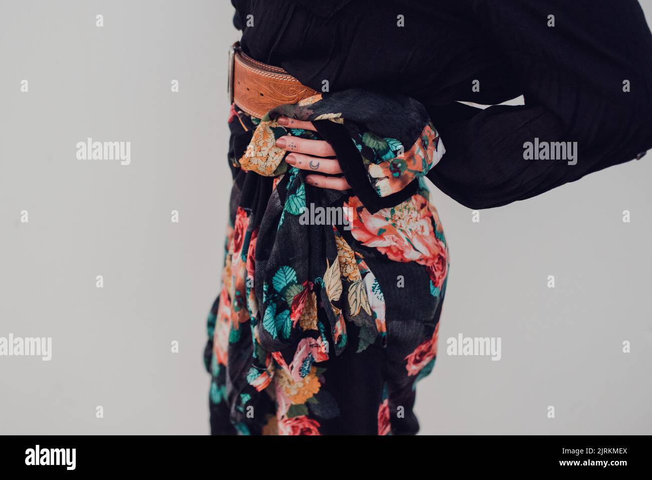 Seitenansicht von Crop trendy schlanke Frau in schwarz gestrickt Pullover und bunten Rock in Zusammensetzung mit braunem Ledergürtel stehend mit Hand auf Hüfte Agai Stockfoto