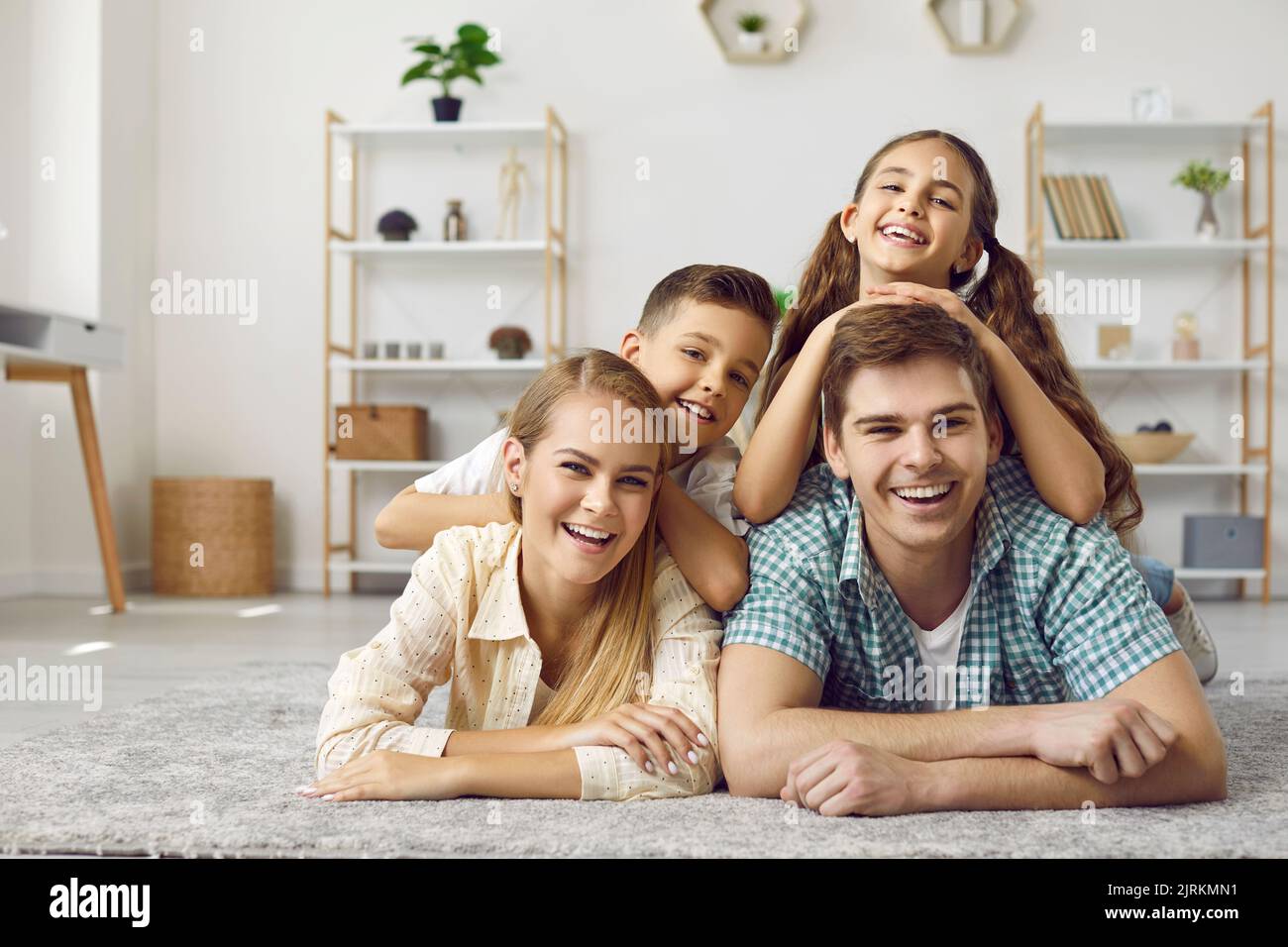 Portrait von positiver Mutter, Vater, Sohn und Tochter, die im Wohnzimmer auf dem Teppich liegen. Stockfoto