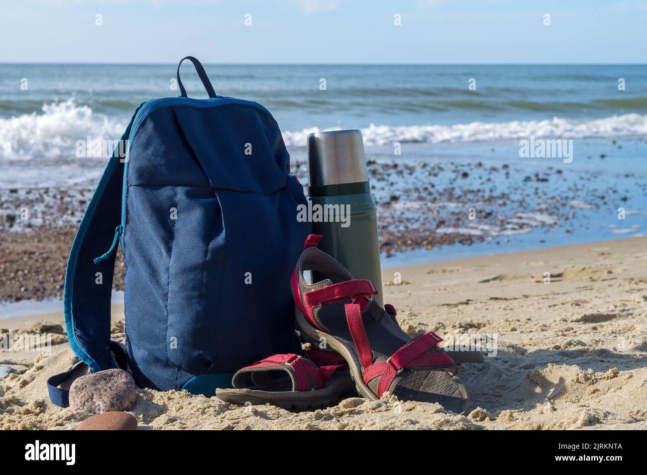 Eine Thermoskanne Tee und ein Rucksack vor dem Hintergrund der Natur. Tee trinken an der Küste. Spaziergang entlang der Küste. Stockfoto