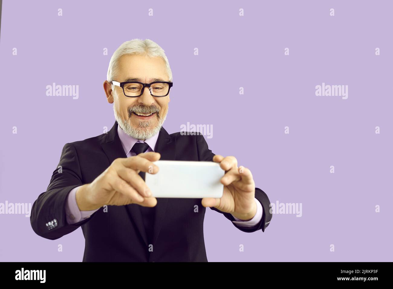 Fröhlicher Geschäftsmann macht Selfie auf Handy auf pastellviolettem Hintergrund. Stockfoto