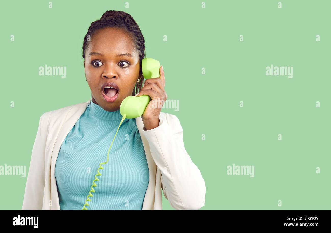 Staunende dunkelhäutige junge Frau, die auf einem Festnetztelefon spricht, isoliert auf hellgrünem Hintergrund. Stockfoto