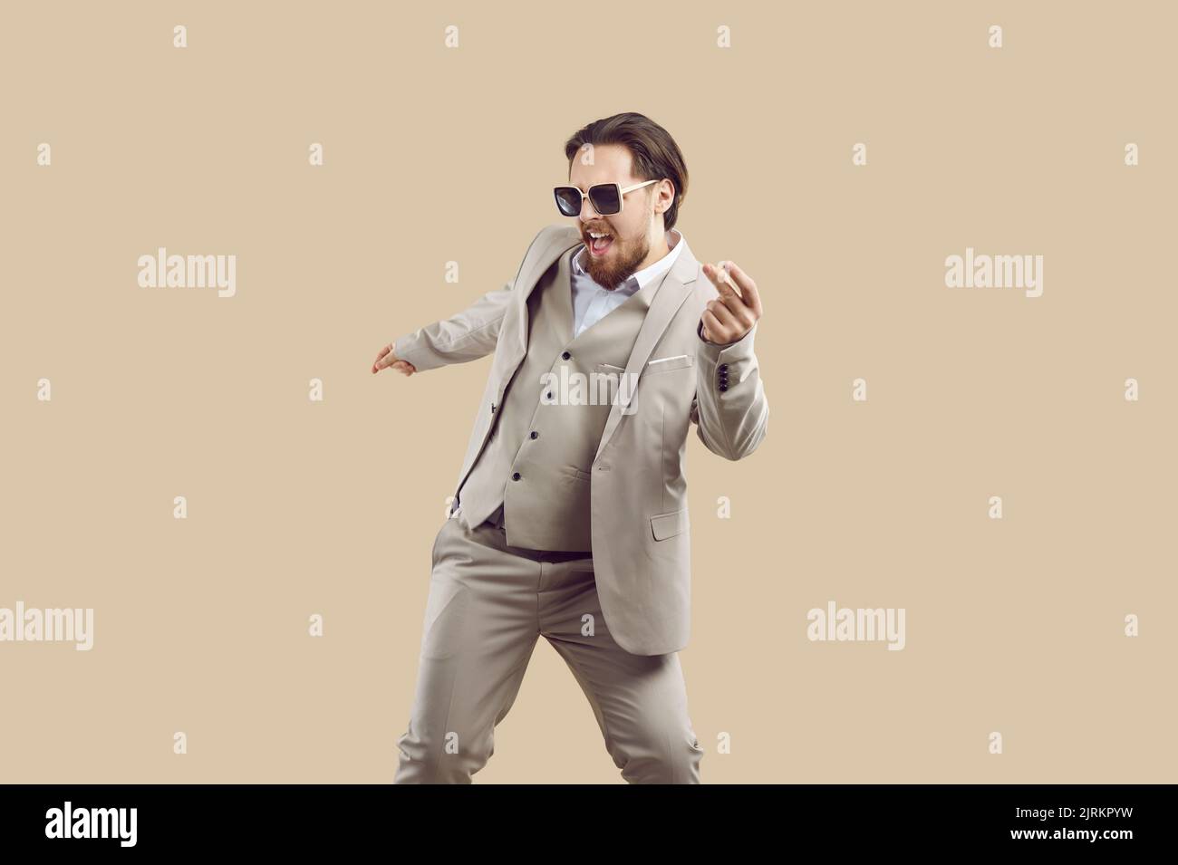 Fröhlicher, cooler Mann im dreiteiligen Anzug freut sich und hat Spaß beim Tanzen auf beigem Hintergrund. Stockfoto
