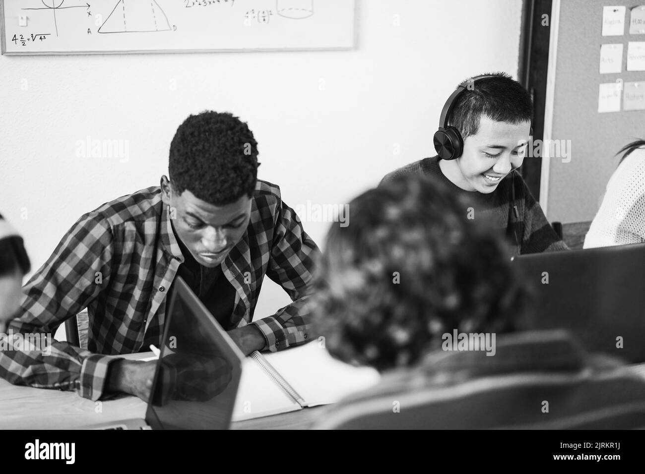 Multirassische Schüler mit Laptop-Computern während des Studiums zusammen in der Schule - Fokus auf asiatische Kerl Gesicht - Schwarz-Weiß-Schnitt Stockfoto